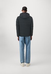 Sort pufferjakke med horisontale quiltede mønster og hætte, parret med lyseblå løstsiddende jeans og hvide sneakers.