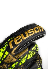 Guanto da portiere nero e verde neon con motivi geometrici dorati e il nome del marchio "reusch" sulla fascia del polso.