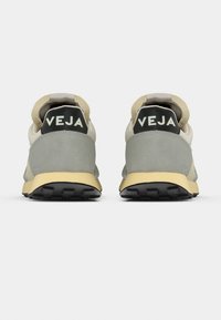 Γκρι και μπεζ αθλητικά παπούτσια με επάνω μέρος από σουέτ και ύφασμα, κίτρινη σόλα σε αντίθεση και μαύρη επωνυμία 'VEJA' στη φτέρνα.