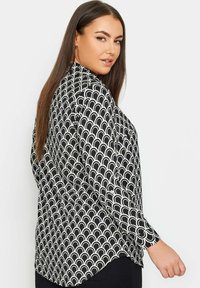Czarna i biała bluzka z falistym wzorem, długimi rękawami i zaokrąglonym dołem. Materiał ma gładką teksturę.