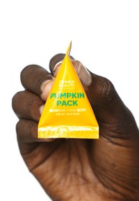Geel driehoekig verpakkingsmateriaal met het label "PUMPKIN PACK" en "ZOMBIE BEAUTY" in vette tekst. Gladde textuur, plastic materiaal, vastgehouden in een hand.