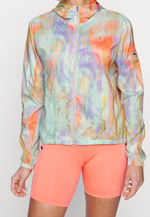 Persoon die een pastel tie-dye zip-up hoodie met capuchon draagt en fel koraalkleurige aansluitende sportshorts.