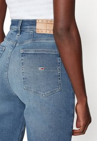 Džínové kalhoty s vysokým pasem v modré barvě se hladkou texturou, s koženou nášivkou na zadní straně s embosovaným nápisem "TOMMY JEANS" a malým logem na kapse.