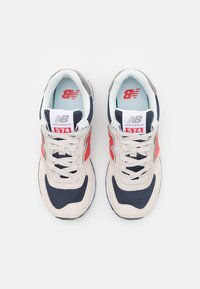 Beige und marineblaue Sneakers aus Mesh- und Wildledermaterialien. Verfügt über reflektierende Akzente, ein markantes "N"-Logo und eine hellblaue Innenauskleidung. Stil 574.