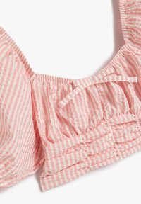 Rosa gestreifte Bluse mit gerafftem Stoff, mit elastischen Ärmeln und einem kleinen Schleifendetail. Leichtes und strukturiertes Baumwollmaterial.