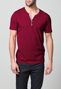 Vínová košile s krátkým rukávem a výstřihem do V, která má knoflíkovou légu a pruhovaný akcent na krku. Měkká tkanina a přiléhavý střih.