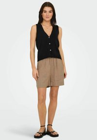 Top negro de punto sin mangas con escote en V y cierre de botones, combinado con pantalones cortos color beige. Diseño sencillo y textura suave. Sandalias negras completan el look.
