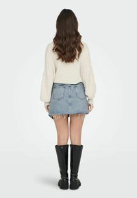 Pulover iz volnenega materiala v kremni barvi, v kombinaciji z modrim jeans mini krilom z raztrganimi robovi in črnimi visokimi čevlji do kolen z debelim again.