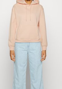 Lichtroze hoodie met een voorzak, geribbelde manchetten en een ontspannen pasvorm, gecombineerd met lichtblauwe wijduitlopende jeans.