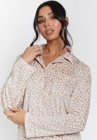 Camisa de pana beige con un patrón de leopardo, presenta un cuello, mangas largas y botones en la parte frontal. Tejido texturizado con un brillo sutil.