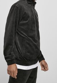 Svart zip-up jacka i mjukt, texturerat tyg. Har två sidofickor, ribbade manchetter och elastisk midja.