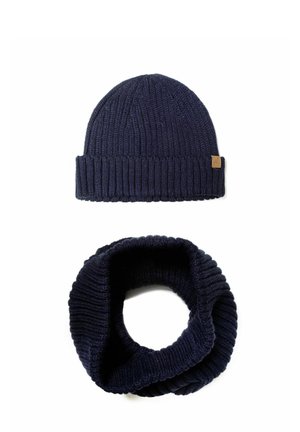 Navyblaue Strickmütze mit geripptem Muster und einem kleinen Lederetikett; passender navyblauer Strick-Infinity-Schal mit ähnlichem Rippdesign.