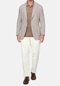 Ljusgrå rutigt kavaj över en brun polo skjorta, matchat med vita byxor och bruna snörskor. Strukturerad design med två knappar.