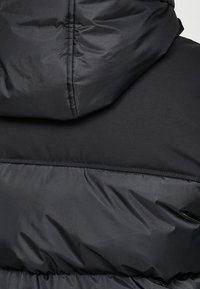 Gros plan sur une veste noire matelassée avec une capuche matelassée et des coutures horizontales cousues à l'arrière.