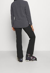 Svarta utomhusbyxor, grå fleecejacka och svarta tekniska stövlar. Slät textur, skräddarsydd passform, rundad nederkant och funktionell design.