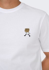 White cotton t-shirt featuring a small embroidered design of a person carrying a stack of round items, with black and yellow detailing.