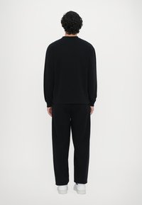 Svart hettegenser og bukser, med lange ermer, avslappet passform og ribbestrikkede mansjetter. Glatt tekstur, enkelt design, kombinert med hvite joggesko.