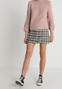 Jasnoróżowy sweter z dzianiny o fakturze falistego wzoru, zestawiony z czarno-białą spódnicą w kratę i czarnymi wysokimi trampkami.