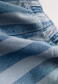 Blå och grå randigt tyg med en mjuk denimtextur, med synliga sömmar längs kanterna och ett vågigt fall.