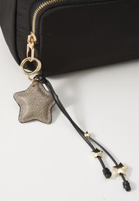 Sac noir avec une fermeture éclair dorée et un porte-clés en forme d'étoile. Le porte-clés a une texture grise et inclut de petits accents d'étoiles dorées.