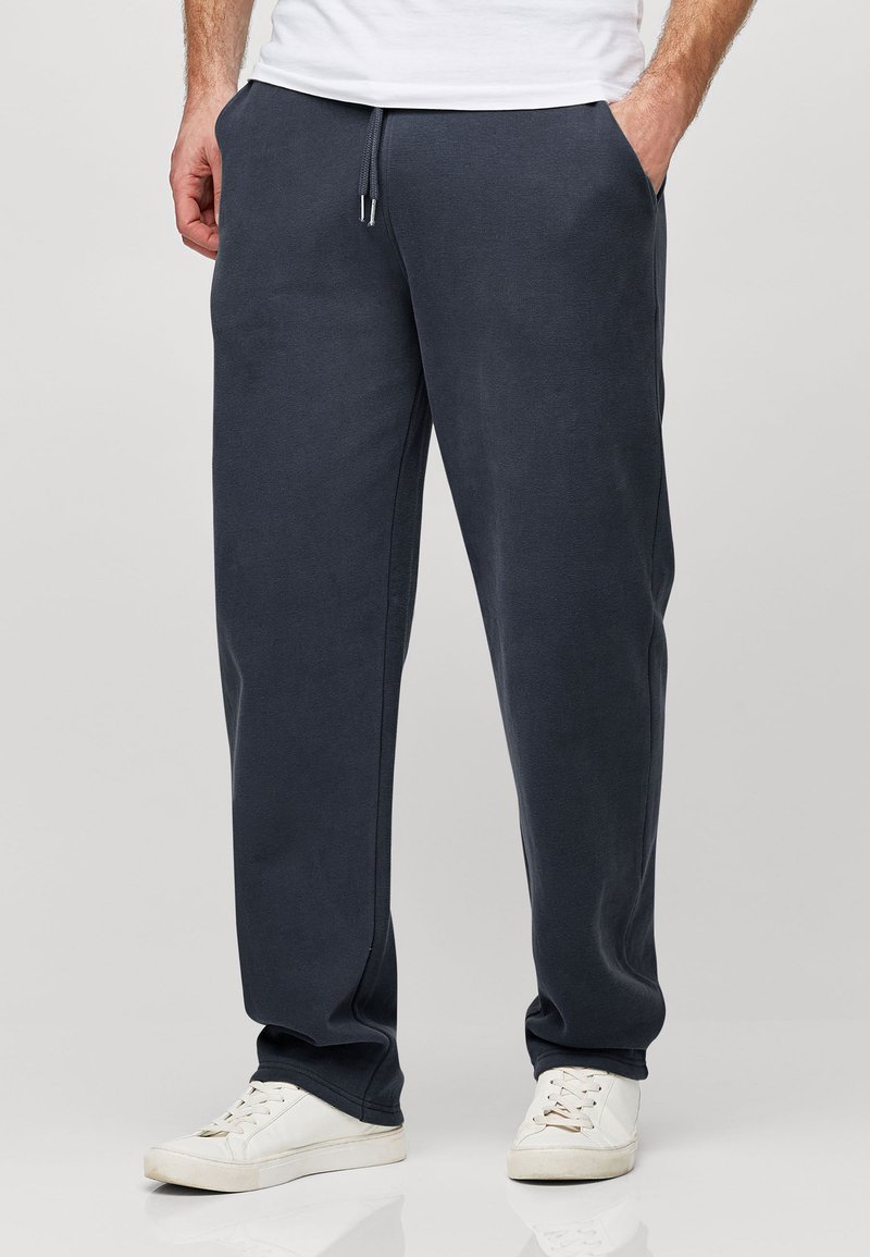 Pantalones de chándal azul marino con cintura elástica, cordón ajustable, bolsillos laterales y un corte holgado, combinados con zapatillas blancas.