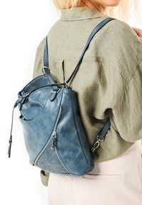 Sac à dos en cuir bleu avec un motif géométrique texturé sur un côt é, des bretelles et plusieurs poches zippées.