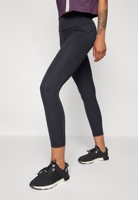 Fekete sport leggings sima varrással és elasztikus derékkal rendelkeznek, fekete edzőcipővel párosítva.