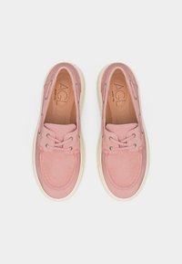 Ζευγάρι ροζ μοκασίνια από σουέτ με λευκές λαστιχένιες σόλες και λεπτομέρειες με κορδόνια, φαίνονται από πάνω σε λευκό φόντο.