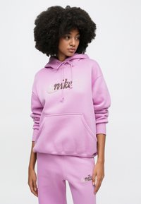 Rosa hettegenser i bomull med snorer og et sølvfarget logo; har en lomme foran. Kombinert med matchende joggebukser som også har logoen.