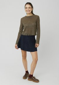 Top métallique bronze à manches longues avec un col rond, associé à une jupe bleu foncé avec une subtile touche de paillettes. Chaussures marron à semelles épaisses.