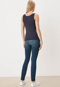 Navy tanktop van katoen, aansluitende pasvorm met brede armsgaten, gecombineerd met donkerblauwe skinny jeans en witte sneakers met zilveren details.
