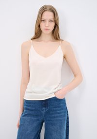 Light beige camisole with thin straps, V-neck design, made from smooth fabric, complemented by blue wide-leg jeans.