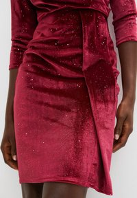 Abito in velluto bordeaux con maniche a tre quarti; presenta accenti argentati sparsi e un design drappeggiato con dettaglio vita legato.
