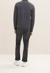 Felpa grigio scuro con collo alto, polsini e orlo a coste, abbinata a jeans scuri e sneakers bianche, vista da dietro.