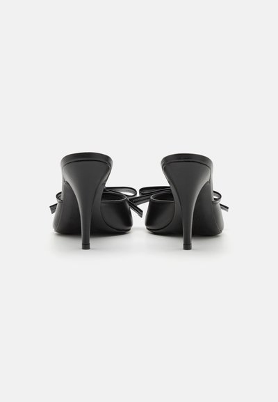 Sorte højhælede sko med en glat læderoverflade, spids tå og en dekorativ sløjfedetalje på hver hæl. Slankt og elegant design.