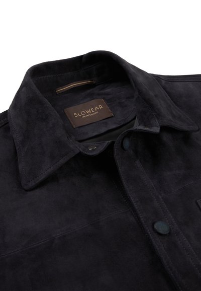 Czarna zamszowa kurtka z szerokim kołnierzem i zapinana na guziki, z brązową metką wewnątrz z napisem "SLOWEAR MONTEODORO".