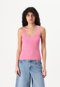 Rosa ribbet tanktopp med dyp V-hals og brede stropper, parret med lyseblå, avslappede jeans. Stoffet ser mykt og elastisk ut.