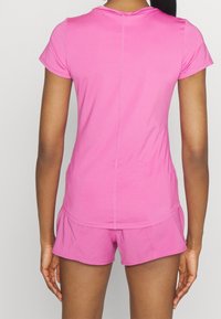 Rosa atletisk tröja med korta ärmar, tillverkad av lättviktig tyg, kombinerad med matchande shorts; har en mjuk textur och en åtsittande design.