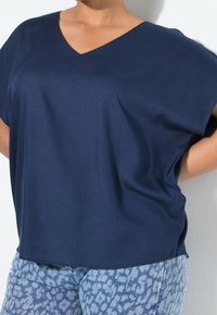 Haut bleu marine à col en V en tissu léger, avec des manches courtes et une coupe décontractée. Associé à un jean bleu à motifs.