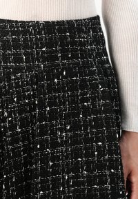 Black and white textured skirt featuring a woven pattern with a grid design and pockets, made from a thick fabric material.