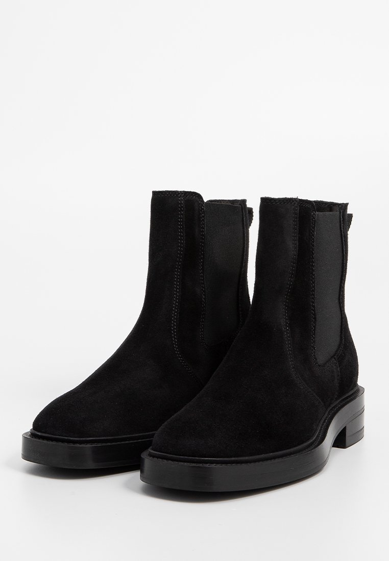 Stivaletti neri in suede, con pannelli elastici laterali, punta tonda e suola in gomma nera a contrasto. Texture liscia, design semplice, dettagli minimal.