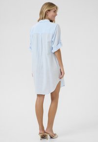 Robe chemise bleu clair à manches courtes, au design décontracté, fabriquée en tissu texturé avec des manches retroussées et un ourlet arrondi.