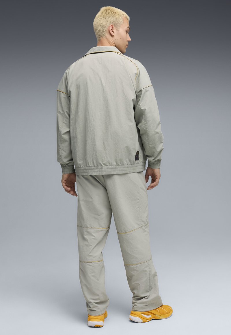 Veste légère gris clair avec des poignets et un ourlet élastiques, associée à un pantalon gris assorti avec des accents jaunes et des chaussures de sport jaunes.