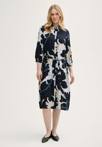 Marineblaues Floral-Kleid mit Druckknopfverschluss, Dreiviertelärmeln, tailliertem Schnitt und fließendem Design mit cremefarbenen und hellblauen Akzenten.