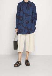Chemise marine à boutons avec un grand motif floral, associée à un pantalon large crème et des sandales noires. Comprend un sac fourre-tout noir.