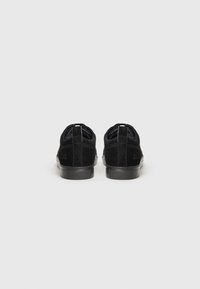 Black suede sneakers with a textured finish, round toe, flat rubber sole, and a looped heel tab for easy wear. Minimalist design.