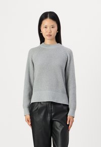 Maglione grigio a maglia con un design testurizzato, polsini e orlo a costine, e scollatura rotonda, abbinato a pantaloni di pelle nera.