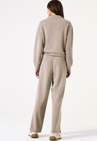 Beige bijpassende sweater en wijde broek, gemaakt van zacht materiaal, met een relaxte fit, geribde manchetten en achterzakken op de broek.