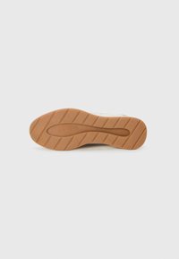 Semelle d'une sneaker avec un bas en caoutchouc, texturé avec des nervures et des rainures, de couleur brun clair avec "ALDO" embossé.