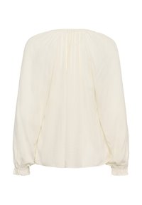 Chemisier blanc à manches longues avec un col froncé et des poignets élastiques, présentant un tissu texturé et une coupe ample et décontractée.